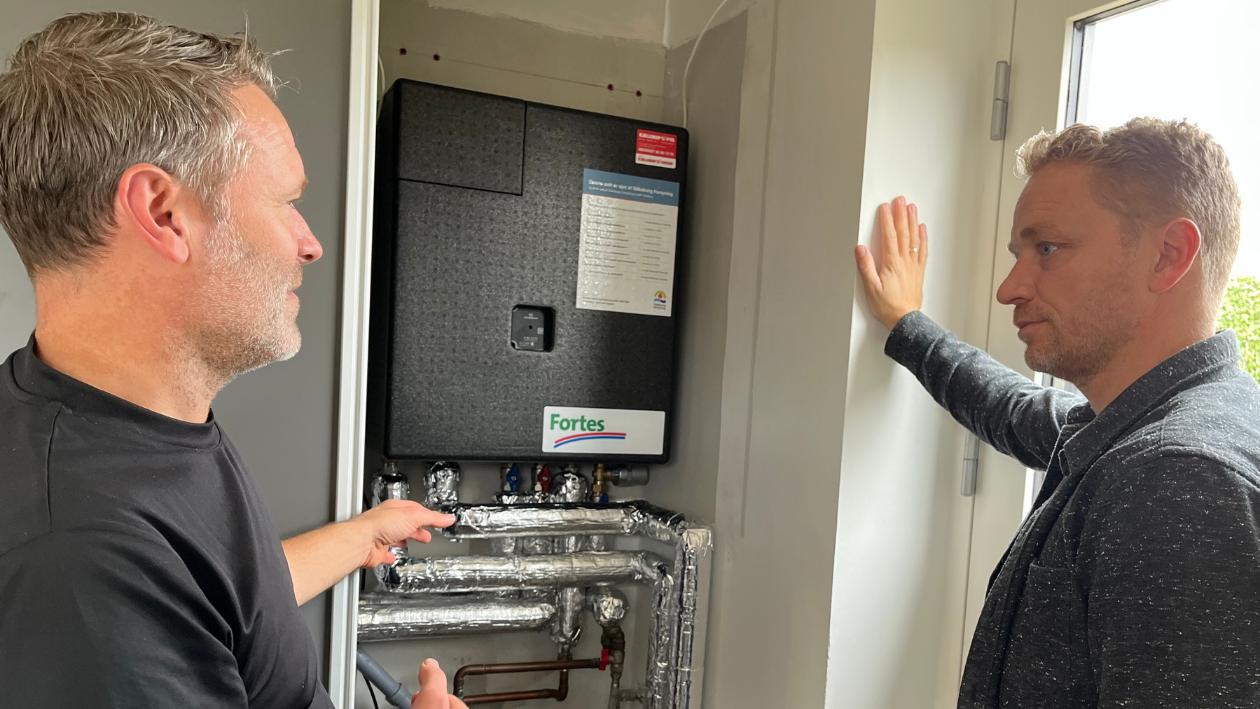 Ole Andersen (tv), håndværker fra Silkeborg Forsynings servicegruppe, fortæller en af de første Unit⁺ kunder, Peder Lille Ravn (th), om hans nye fjernvarmeunit.  Servicetekniker fra Silkeborg Forsyning snakker med kunde Peder Lillelund Ravn om fjernvarme