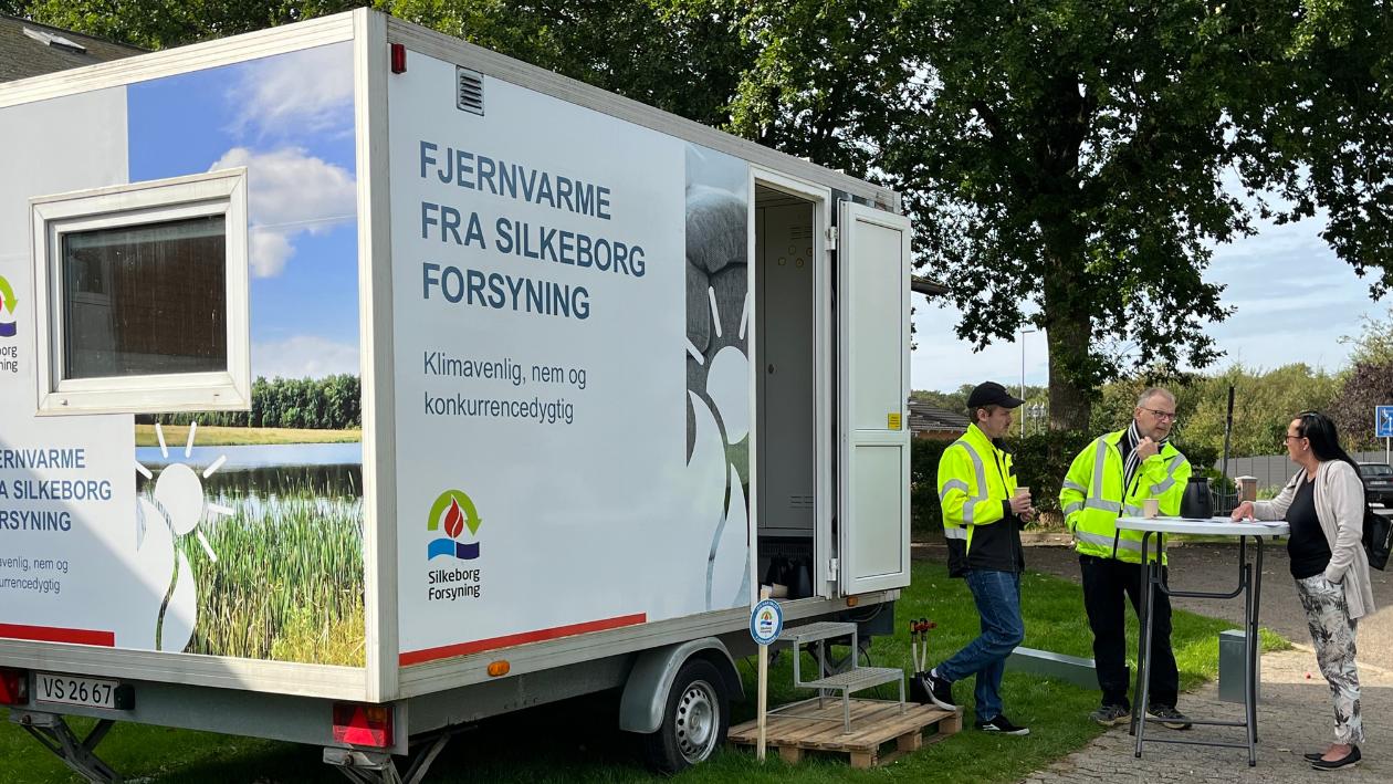 Fjernvarmetraileren på besøg under tilmeldingskampagne i Skægkær og Sejling i efteråret 2023. Fjernvarmetrailer står parkeret ved en skole, hvor to fjernvarmeeksperter taler med en borger